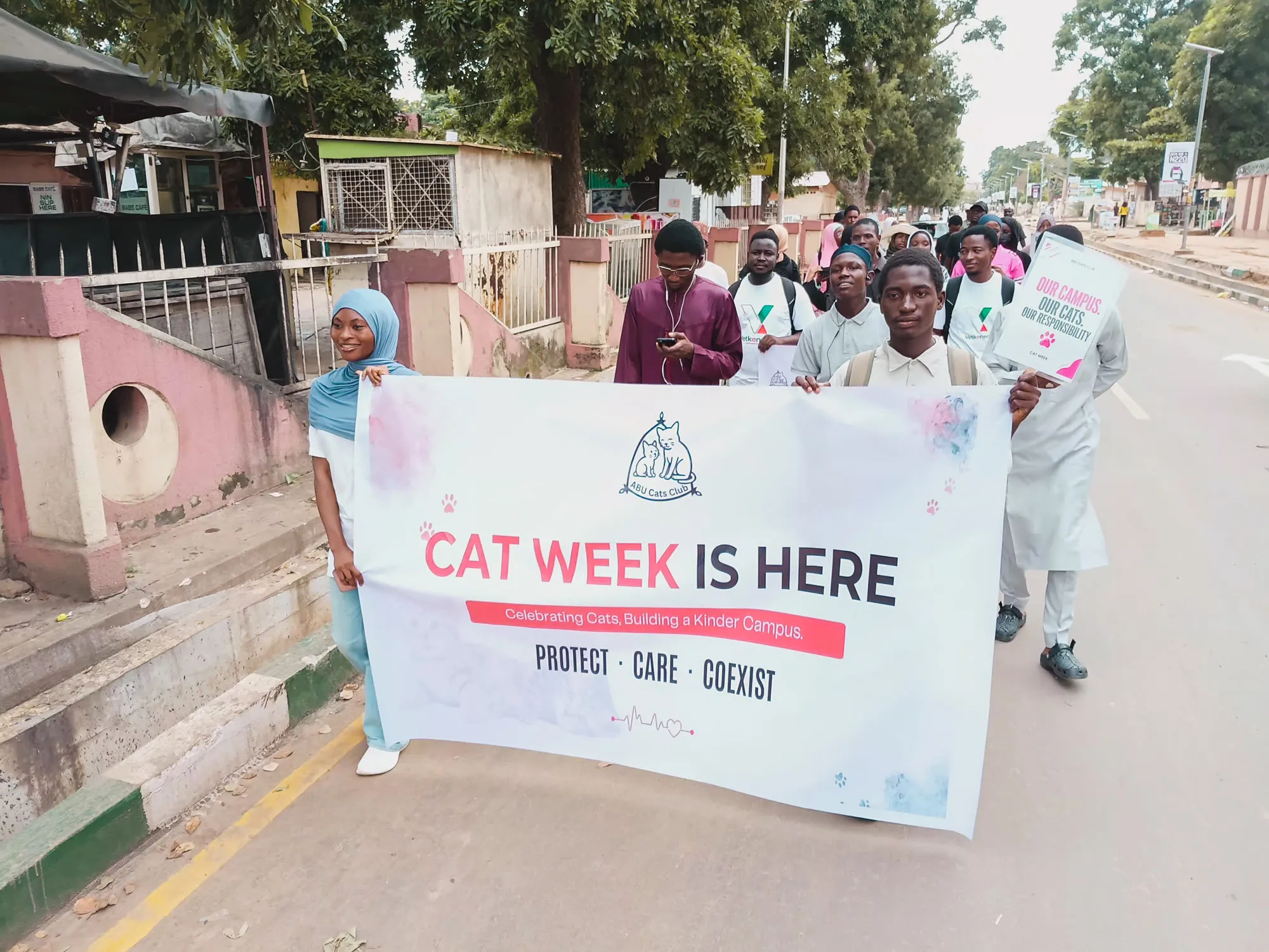 ABU Cats Club members carrying a Cat Week banner along a road on the Samaru campus